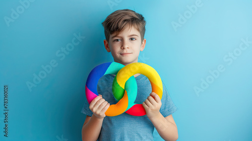 Boy holding colorful infinity symbol, concept of Autism Awareness on pastel blue background