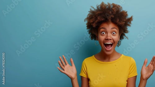 A young African American woman with a fun surprised expression, wearing a yellow shirt against a blue background. Copy space available