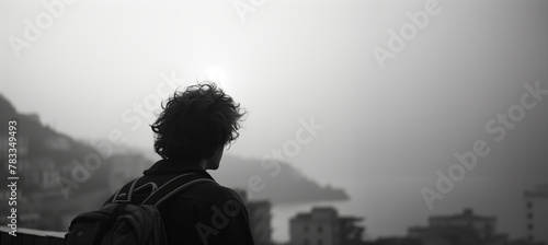 A solitary silhouette of a person looking out towards the sea and a misty coastal town