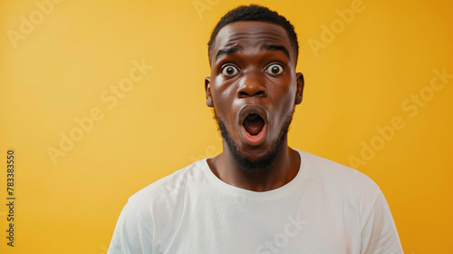 young shocked african american guy in white oversized t-shirt is surprised on yellow isolated background 