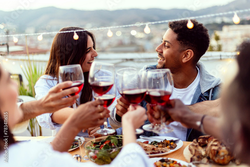 Group of people enjoying summer night dinner party at home terrace. Multiracial friends social gathering reunited together celebrating at rooftop. Summertime concept.