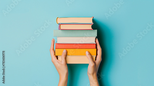 Empilement de livres , mains de femme tenant par dessous une pile de livres nouveaux sur fond bleu clair. Éducation, bibliothèque, science, connaissances, études, échange de livres, passe-temps