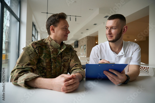 Doctor writing down information on clipboard in presence of serviceman