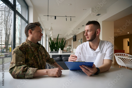 Doctor writing down soldier medical history during primary consultation