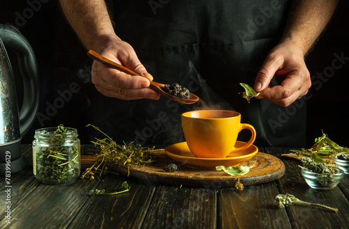 The cook brews healthy tea from medicinal dry herbs. A hand holds a spoon with dry rosehips that need to be added to a yellow cup. Low key concept of traditional medicine.