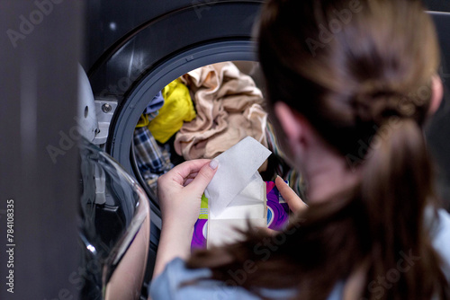 Woman siting in front of a washing machine loading dirty clothes, napkins for washing colored clothes