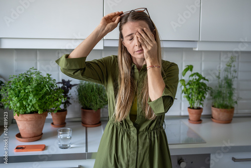 Sleepy woman suffering from chronic fatigue rubbing eyes on kitchen at home. Tired middle aged female feeling bad from lack of rest, headache, lack of energy after party, sleepless night. 