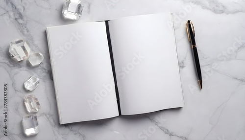 A white note book on a marble table with leaves. 
