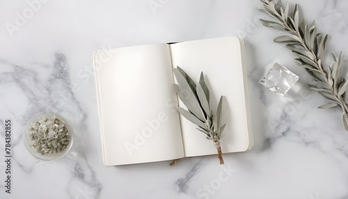 A white note book on a marble table with leaves. 