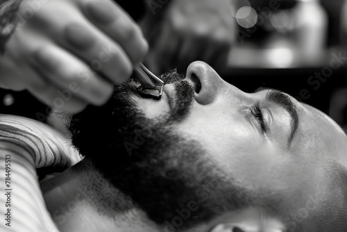 Black and white shot of a man getting a meticulous beard trim with a clipper by a skilled barber for a neat look.