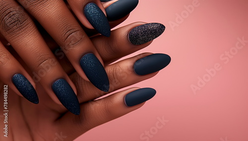 Elegant almond-shaped deep blue glitter and matte manicure on dark skin against a pink background, perfect for beauty concepts