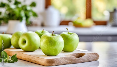 A selection of fresh fruit: green apple, sitting on a chopping board against blurred kitchen background; copy space 