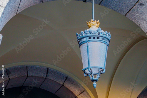 Antique hanging lamp from arched ceiling, metal structure with beautifully crafted details simulating a golden crown, covered in dust, plafond in background