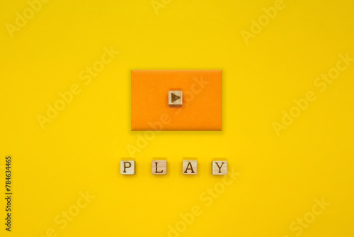 PLAYの単語の上にオレンジの四角い立体的な再生マークのアイコンが並ぶ黄色い背景