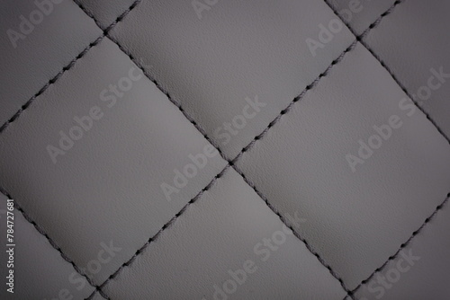 Dark gray contrast thread on natural gray leather car seat close-up