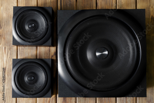 Large cubic subwoofer in a wooden cabinet with metal grille and two audio speakers on a background of natural pine boards. Audiophile concept. Audio system 2.1. Photo