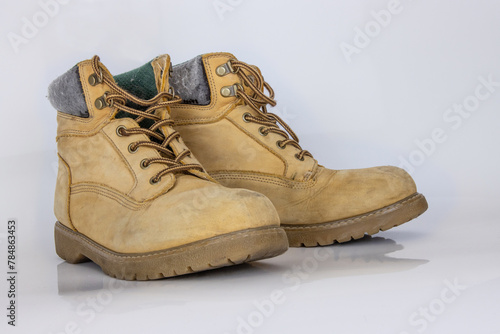 Pair of worn old yellow hiking trekking lace boots Isolated on white glossy surface with beautiful reflection effect. Second hand tourist walking shoes. Side view. Copy Space. White background.