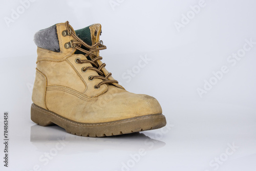 One worn old yellow hiking trekking lace boots Isolated on white glossy surface with beautiful reflection effect. Second hand tourist walking shoes. Side view. Copy Space. White background.
