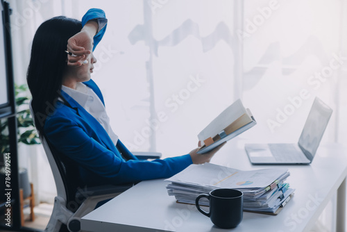 Asian woman feeling migraine head strain.Overworked businesswoman financier while working on laptop and tablet at modern office.