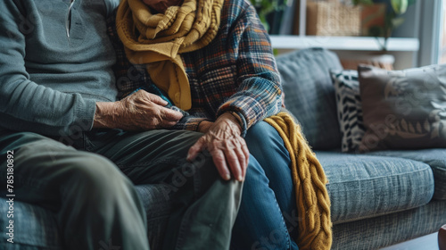 An older couple finds comfort and warmth in each others touch, sitting closely on a couch with a knit blanket