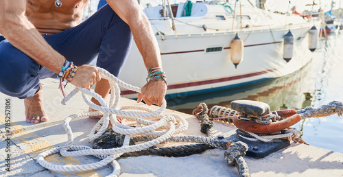 Unrecognizable young adult man tying up a mooring rope at the dock of the yacht marina before setting off to sail