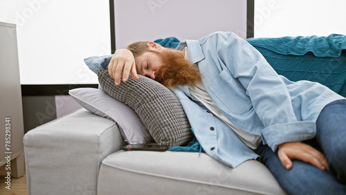 Exhausted young irish man with redhead beard finds comfort relaxing on cozy sofa, deeply sleeping at home in the living room, relishing the relaxation of a well-deserved rest