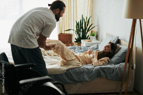 bearded handsome man helping his disabled cheerful wife to stretch muscles while she lying on bed