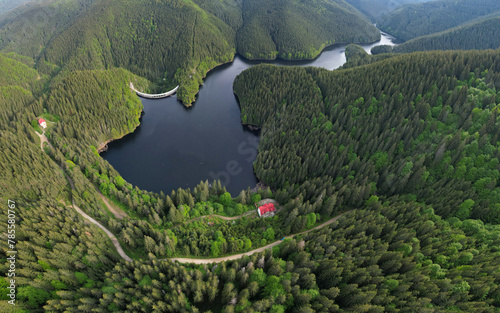 Aerial drone view above Gatu Berbecului lake at sunset. The water is hold by an arched concrete dam, built within the wilderness of Cindrel Massif. Carpathia, Romania.