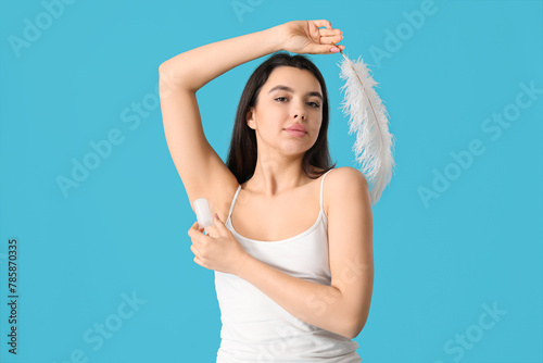 Beautiful young woman with crystal deodorant and feather on blue background