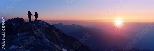  A Couple climber on a mountain peak at dawn that paints the sky with spectacular colors and standing on top of mountain with backpacks on morning sky is a bright orange and the sun peeking over the 