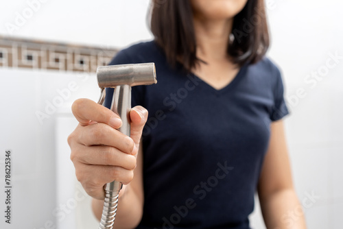 Hand female holding injecting rinse spray hose in the toilet. Young woman on a toilet sitting by using a bidet shower. Hygiene concept