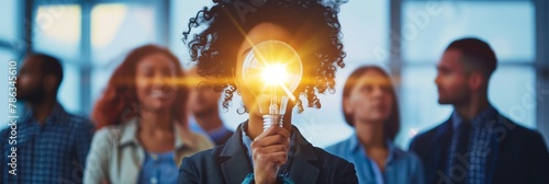 Individual holding a lighted bulb in front, concept of idea creation with peers in background