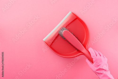 Hand in pink rubber glove holding dustpan and brush