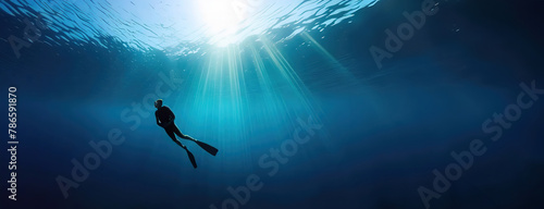 A diver explores the ocean depths, sunlight beams through water. Serenity envelops as the lone figure is submerged in the marine blue expanse.