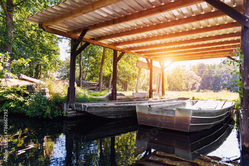 Old metal boat moored under shed shelter wooden canopy rustic boathouse at countryside in Spreewald canal national biosphere reserve house. Scenic Vintage water transport warm morning sunrise