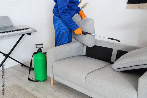 Male worker disinfecting sofa in room