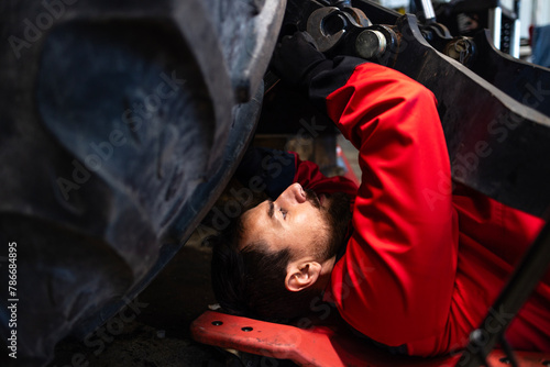 Mechanic lying under tractor repairing agricultural machine.