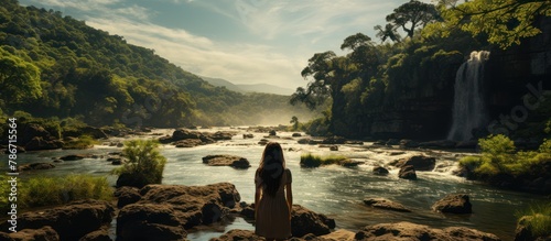 silhouette of woman standing on a cliff by a wild river and waterfall, enjoying the view