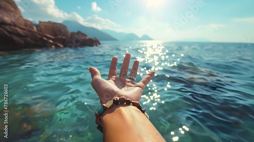 A traveler girl's hand adorned with bracelets pointing towards the sea on a sunny day.