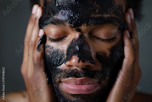 Close-up portrait of a man with eyes closed, applying a detoxifying charcoal mask on his face