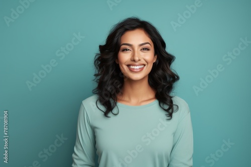 Portrait of a satisfied indian woman in her 30s sporting a long-sleeved thermal undershirt on soft teal background