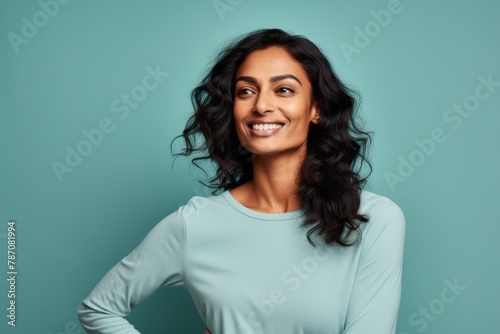 Portrait of a satisfied indian woman in her 30s sporting a long-sleeved thermal undershirt in soft teal background