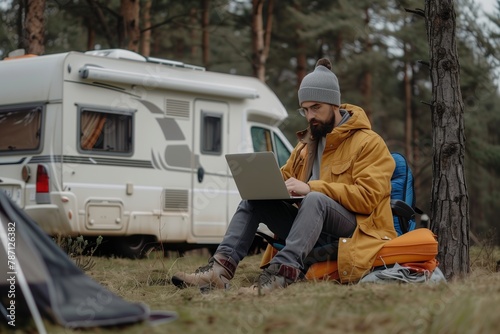 A freelancer lives in a campervan and works outdoors. This scene represents a harmonious combination of work and nature, where a man can enjoy the beauty of the environment without interrupting his wo