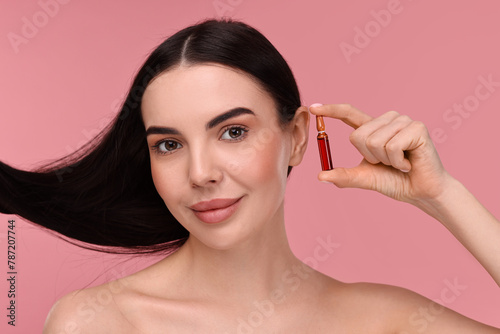 Beautiful young woman with long healthy hair holding ampoule on pink background
