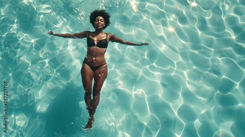 Black woman in elegant swimsuit swimming in crystal-clear pool from overhead perspective