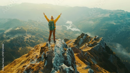 A person stands triumphantly on a mountain summit with arms raised in victory