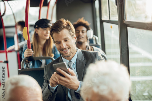 Smiling young adult businessman using smartphone on the bus