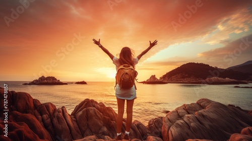 Happy woman raising arms up enjoying sunset on the beach - Delightful traveler standing with hands up looking morning sunrise - Self care, traveling, wellness and healthy life style concept