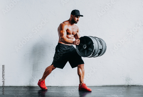 Young strong man bodybuilder posing with big barrel in hand