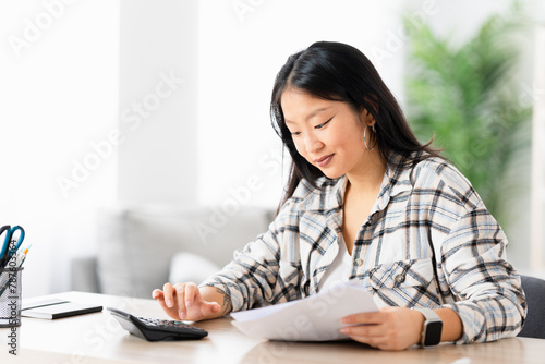 Young chinese woman preparing home budget using calculator sitting in the living room